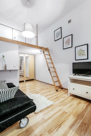 A modern room with a loft bed, a TV, a ladder, and framed cityscape pictures on the wall. - EchoDom 8 Apartments Zygmunta Augusta (Kraków)