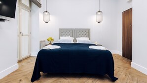 A modern bedroom with a large bed, two bedside tables, a TV mounted on the wall, and a wooden wardrobe. - EchoDom 8 Apartments Zygmunta Augusta (Kraków)