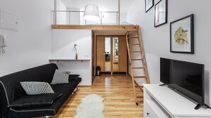 A modern living room with a loft bed, a TV, a black sofa, and a white rug. - EchoDom 8 Apartments Zygmunta Augusta (Kraków)
