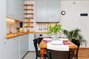 A modern kitchen with white cabinets, a wooden countertop, and a dining table set for two. - EchoDom 8 Apartments Zygmunta Augusta (Kraków)