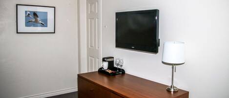A hotel room with a wooden dresser, a flat-screen TV, a framed picture of birds, a coffee maker, and a lamp.