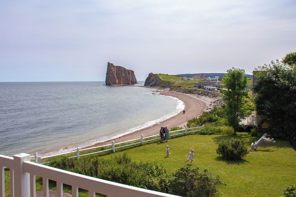 A coastal view with a prominent rock formation, a beach, and a grassy area with a fence.