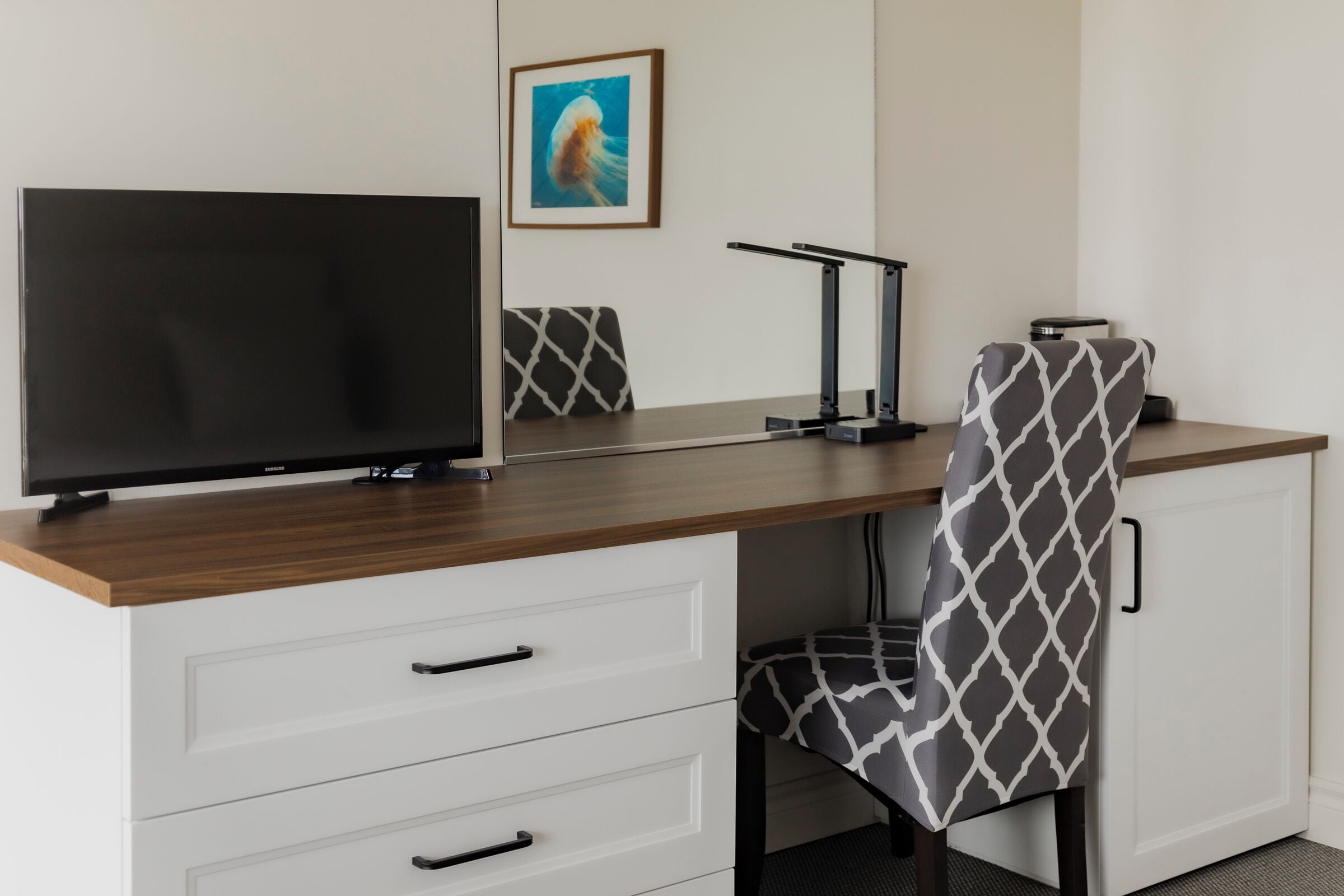 A modern office desk with a flat-screen TV, a lamp, and a patterned chair.