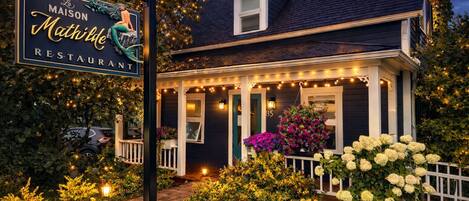Una casa de dos pisos con un porche decorado con luces de cuerda y plantas en macetas.