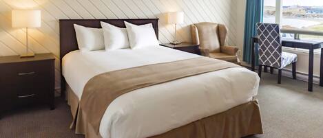 A hotel room with a large bed, two bedside tables with lamps, a desk with a chair, and a view of the outside.