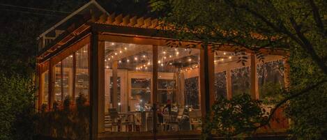 A covered outdoor seating area with string lights, large windows, and a wooden deck.