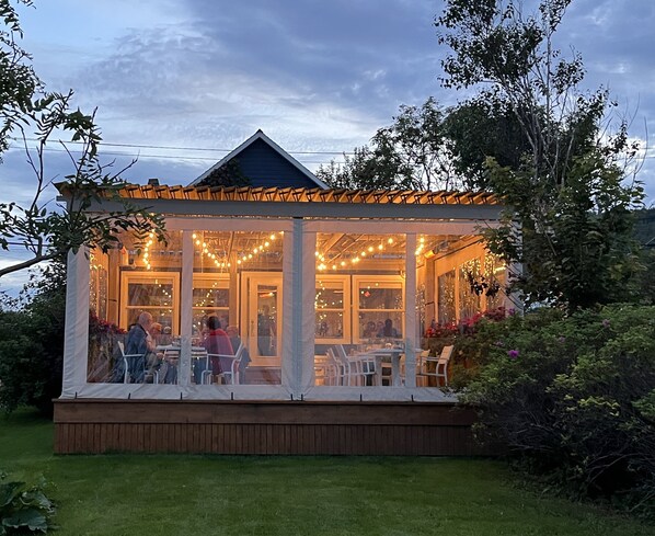 A covered outdoor seating area with string lights, wooden deck, and glass walls.