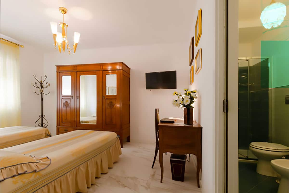 A hotel room with two beds, a wooden wardrobe, a desk with a chair, a television, and a bathroom visible through an open door.