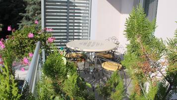 Une table ronde entourée de chaises, de plantes en pot et d’une fenêtre avec des stores.