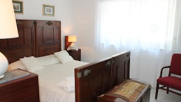 Une chambre à coucher avec un lit en bois, une table de chevet avec une lampe, une chaise et une fenêtre ornée de rideaux légers.