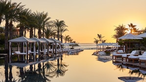A serene pool area with lounge chairs and umbrellas, surrounded by palm trees and a sunset view. - Chileno Bay Resort & Residences, Auberge Collection (Cabo San Lucas)