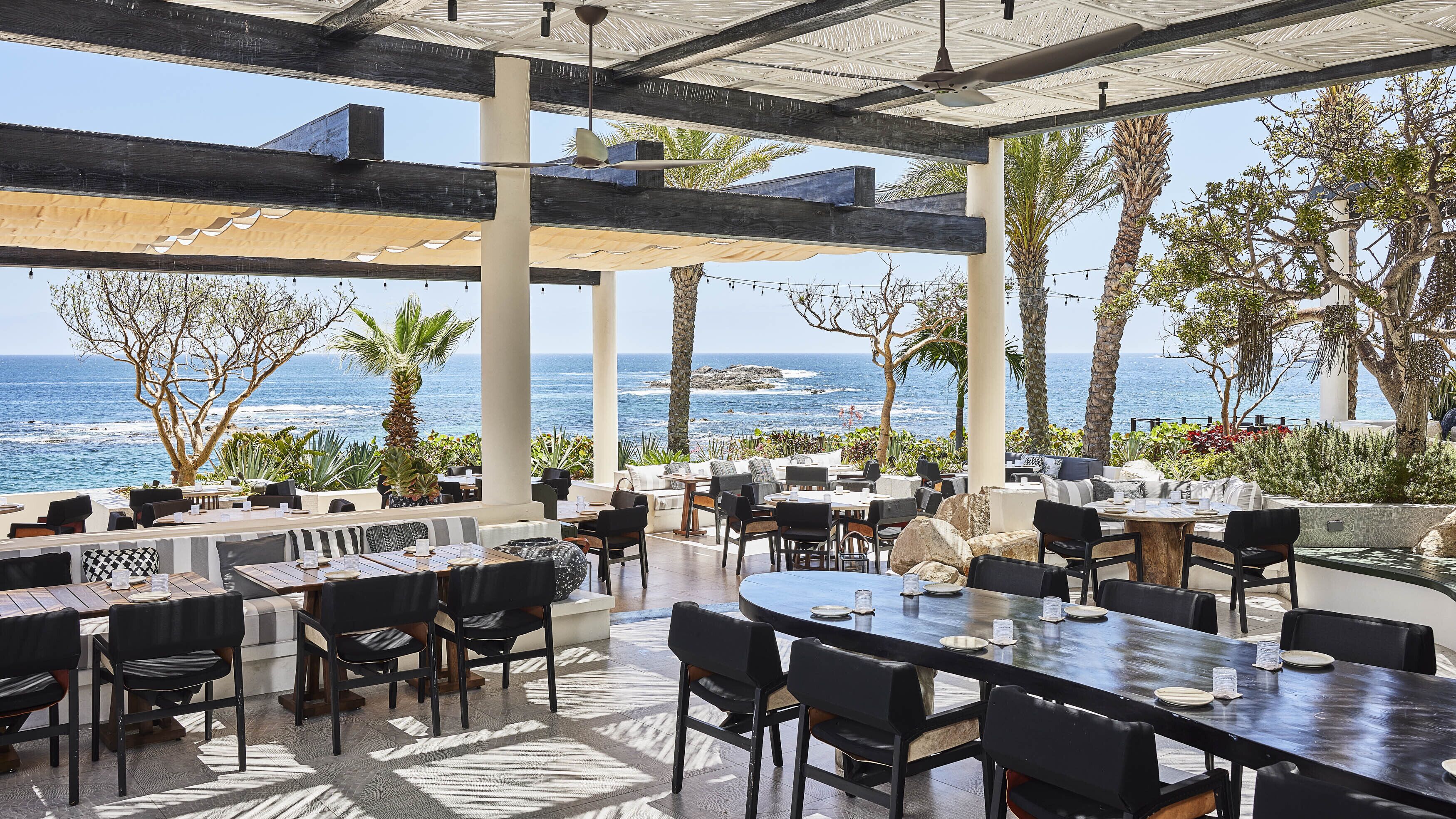An outdoor dining area with tables and chairs, overlooking the ocean.