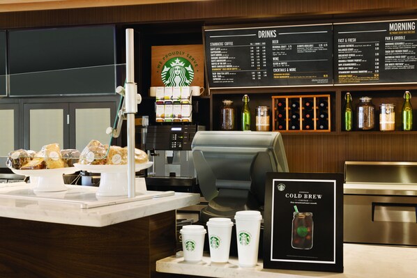 Interior de uma cafeteria Starbucks, com um quadro de menu, máquinas de café e uma vitrine de doces.