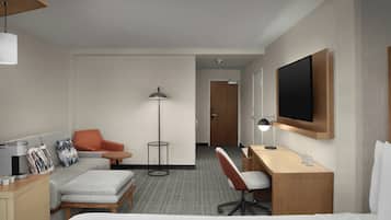A hotel room with a bed, a desk, a chair, a sofa, a coffee machine, a lamp, and a TV.