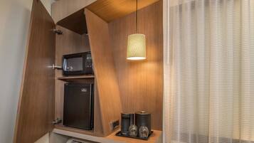 Una kitchenette compacta con microondas, cafetera y cristalería sobre una encimera de madera.