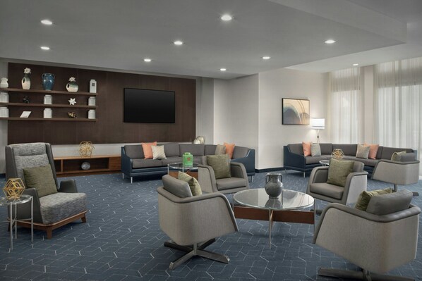 Een moderne hotellobby met een zithoek, een flatscreen televisie en een bijzettafeltje.