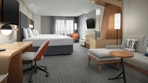 Une chambre d’hôtel moderne dotée d’un grand lit, d’un bureau avec une chaise, d’un canapé, d’une petite table et d’un téléviseur fixé au mur.