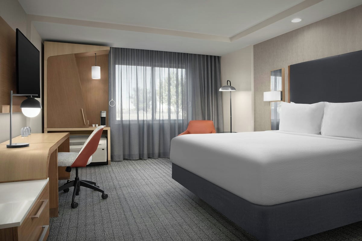 Une chambre d’hôtel avec un grand lit, un bureau avec une chaise, une télévision et une fenêtre avec des rideaux.