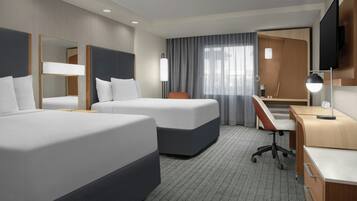 A hotel room with two beds, a desk, a chair, a TV, and a large window with curtains.