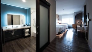 Ein modernes Hotelzimmer mit einem großen Bett, einem eigenen Badezimmer mit Spiegel, einem Schreibtisch und einem Stuhl.