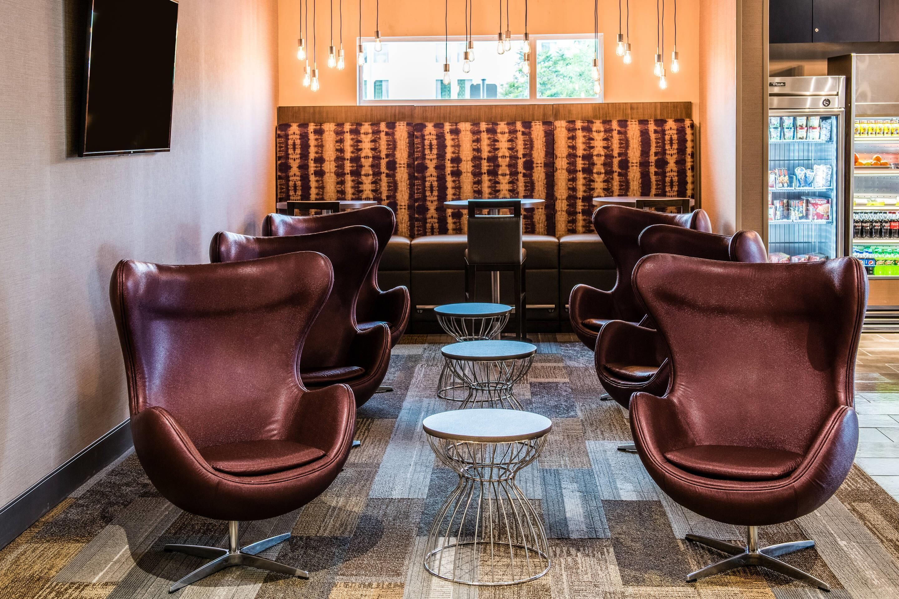 A seating area with leather chairs and tables, a patterned wall, and a refrigerator stocked with beverages.
