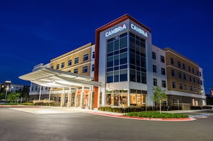 A multi-story hotel with a prominent 'CAMBRIA' sign, a covered entrance, and a parking lot.