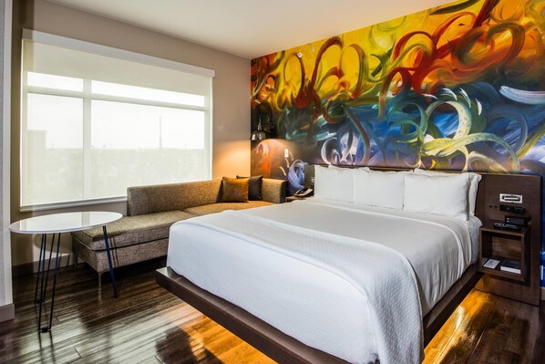 A hotel room with a large bed, a sofa, a small table, and a painting on the wall. - Cambria Hotel McAllen Convention Center (McAllen)