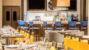 Ein Restaurant mit mehreren Tischen und Stühlen, einer Bar mit verschiedenen Flaschen sowie einem an der Wand befestigten Fernsehbildschirm.