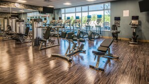 Ein Fitnessstudio mit unterschiedlichen Trainingsgeräten, großen Fenstern und Holzboden.