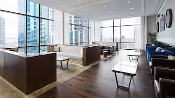 A modern lounge area with a high ceiling, large windows offering city views, and a mix of seating options including sofas and chairs.