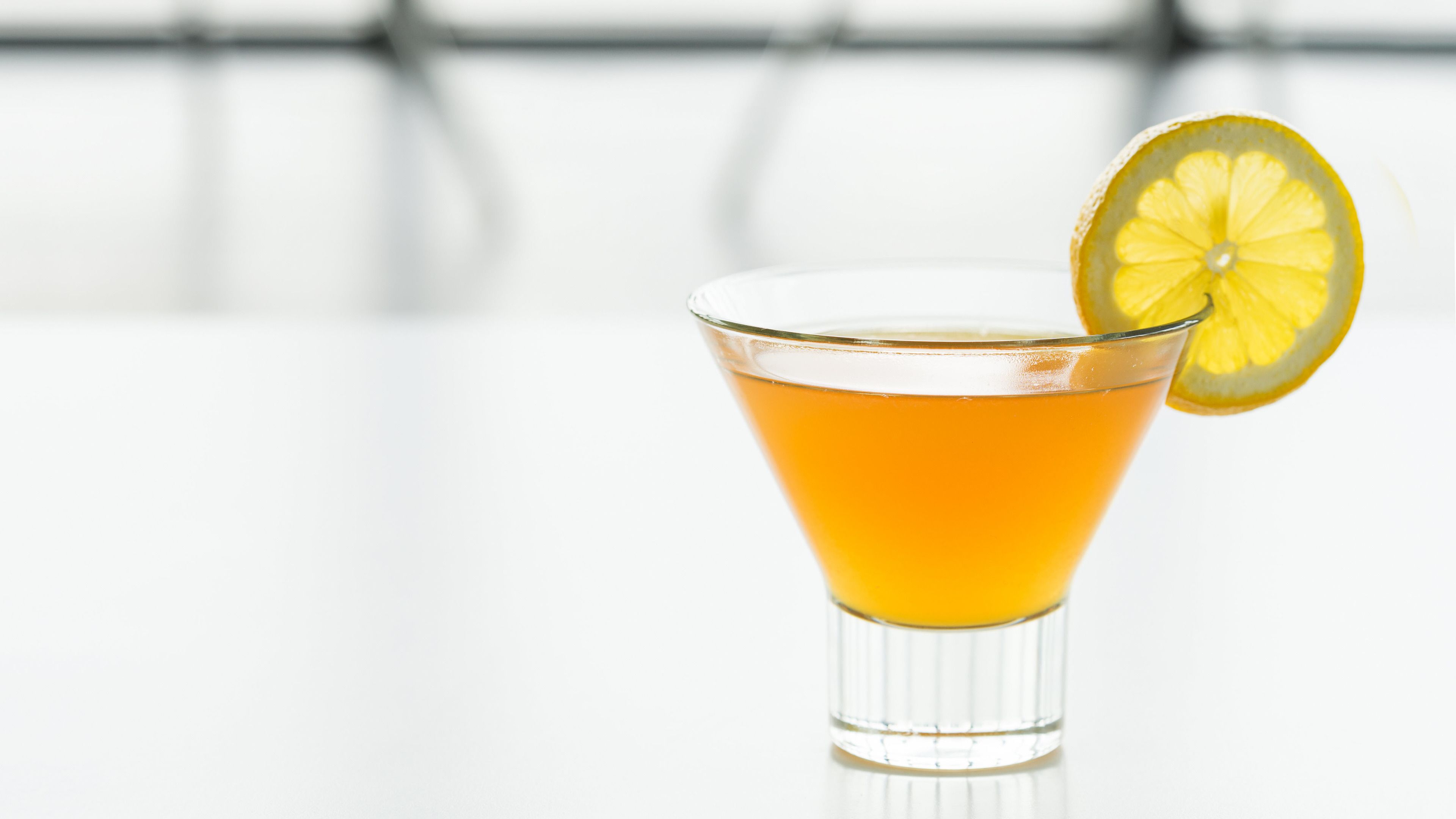 A clear glass cocktail with a lemon garnish on a white surface.