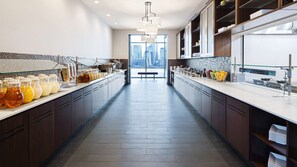 A modern kitchen with a long counter, glass containers of beverages, and a view of the city through large windows. - Hyatt House Jersey City (Jersey City)
