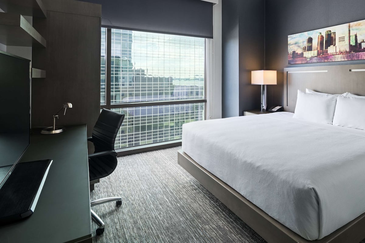 Une chambre d’hôtel avec un grand lit, un bureau avec une chaise, une lampe et un tableau représentant un paysage urbain accroché au mur.
