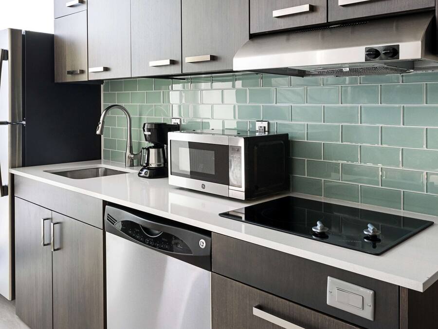 Une cuisine moderne dotée d’appareils électroménagers en acier inoxydable, d’un lave-vaisselle et d’un revêtement mural en carreaux.