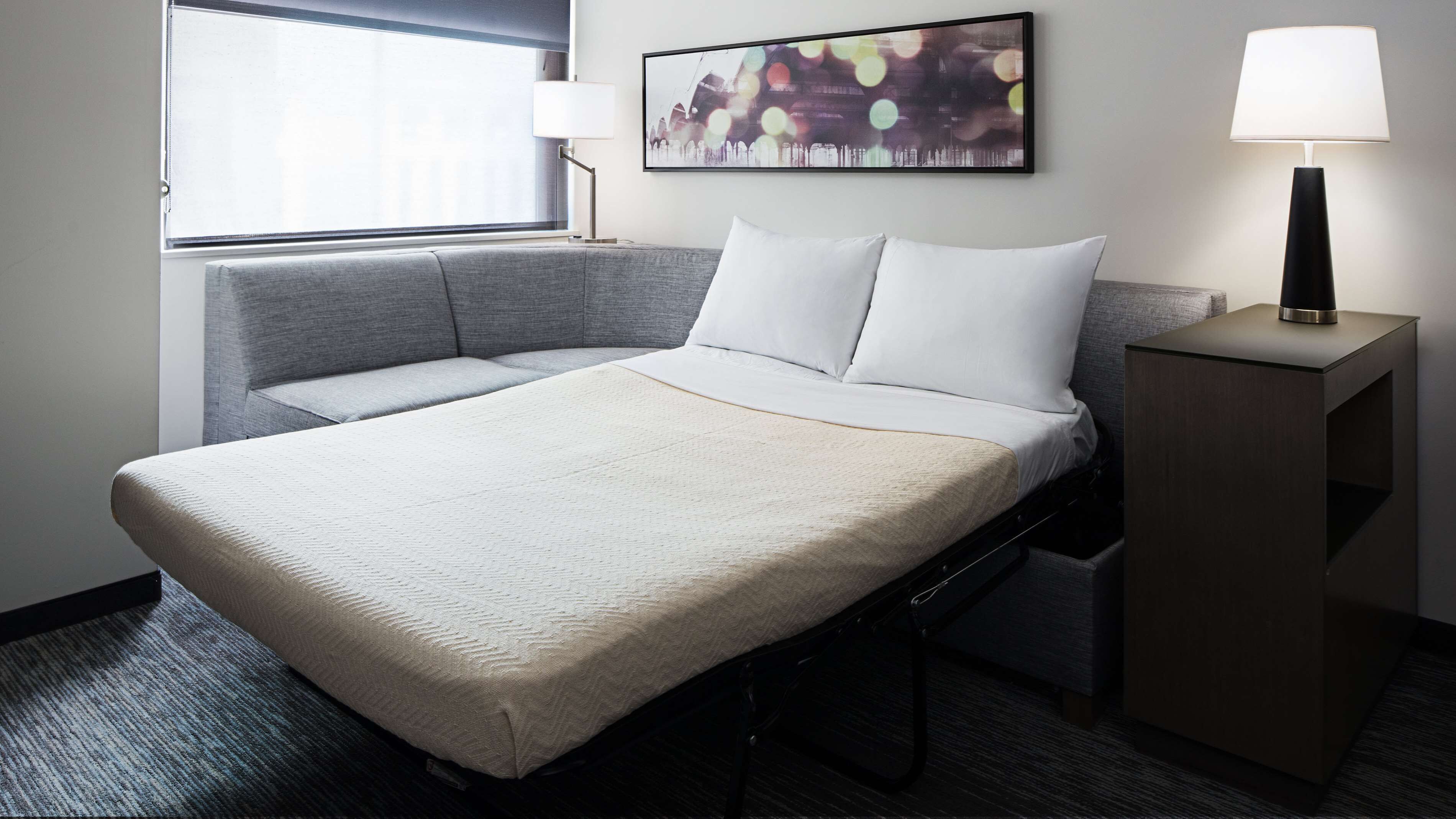 Ein Hotelzimmer mit Bett, Nachttisch, Lampe und Fenster mit Jalousien.