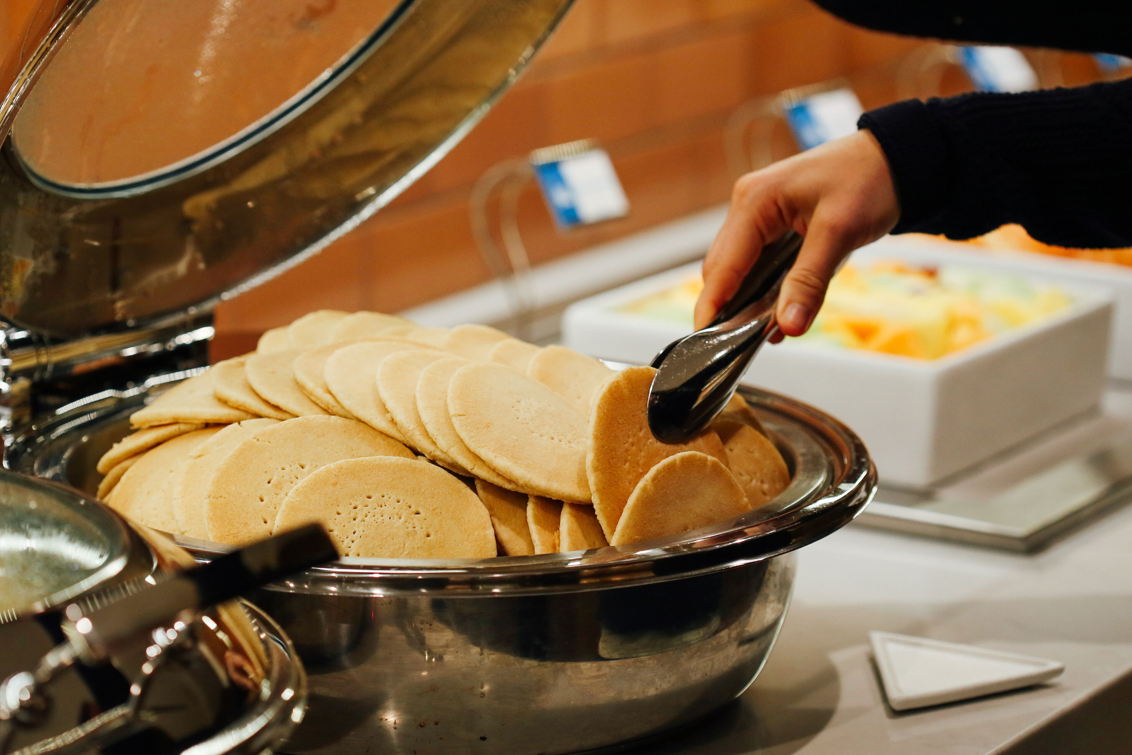 A buffet with a large metal bowl filled with pancakes.