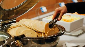 A buffet with a large metal bowl filled with pancakes.