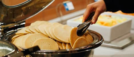 A buffet with a large metal bowl filled with pancakes.