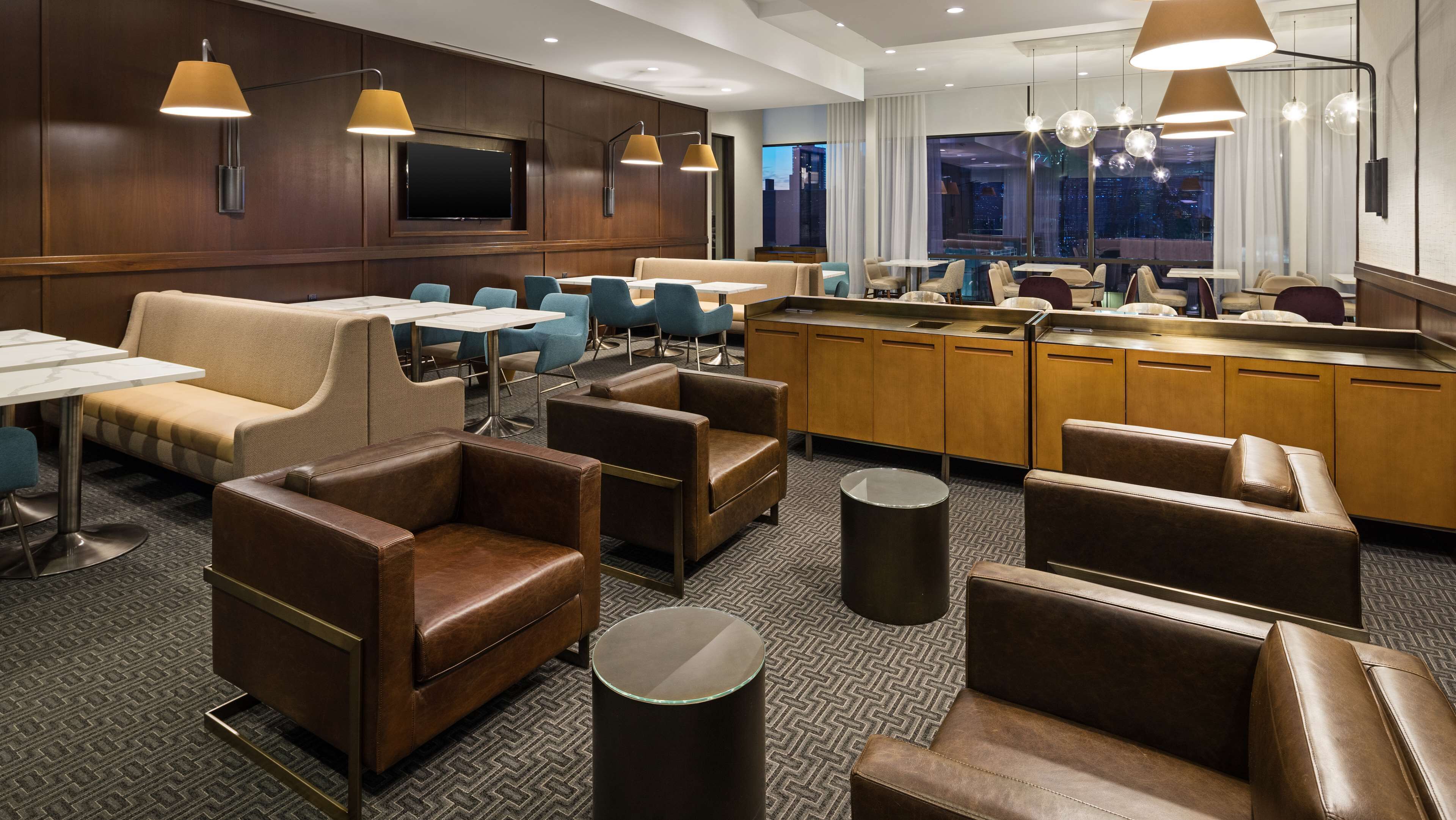 A hotel lobby with leather seating, a bar area, and a large window offering a city view.