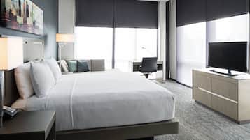 Habitación de hotel con una cama grande, un escritorio con silla, un televisor y una ventana con persianas.