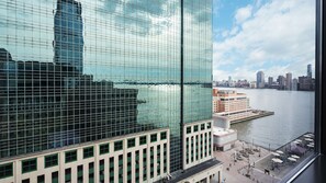 A modern high-rise building with a glass facade reflecting the city skyline and a river. - Hyatt House Jersey City (Jersey City)
