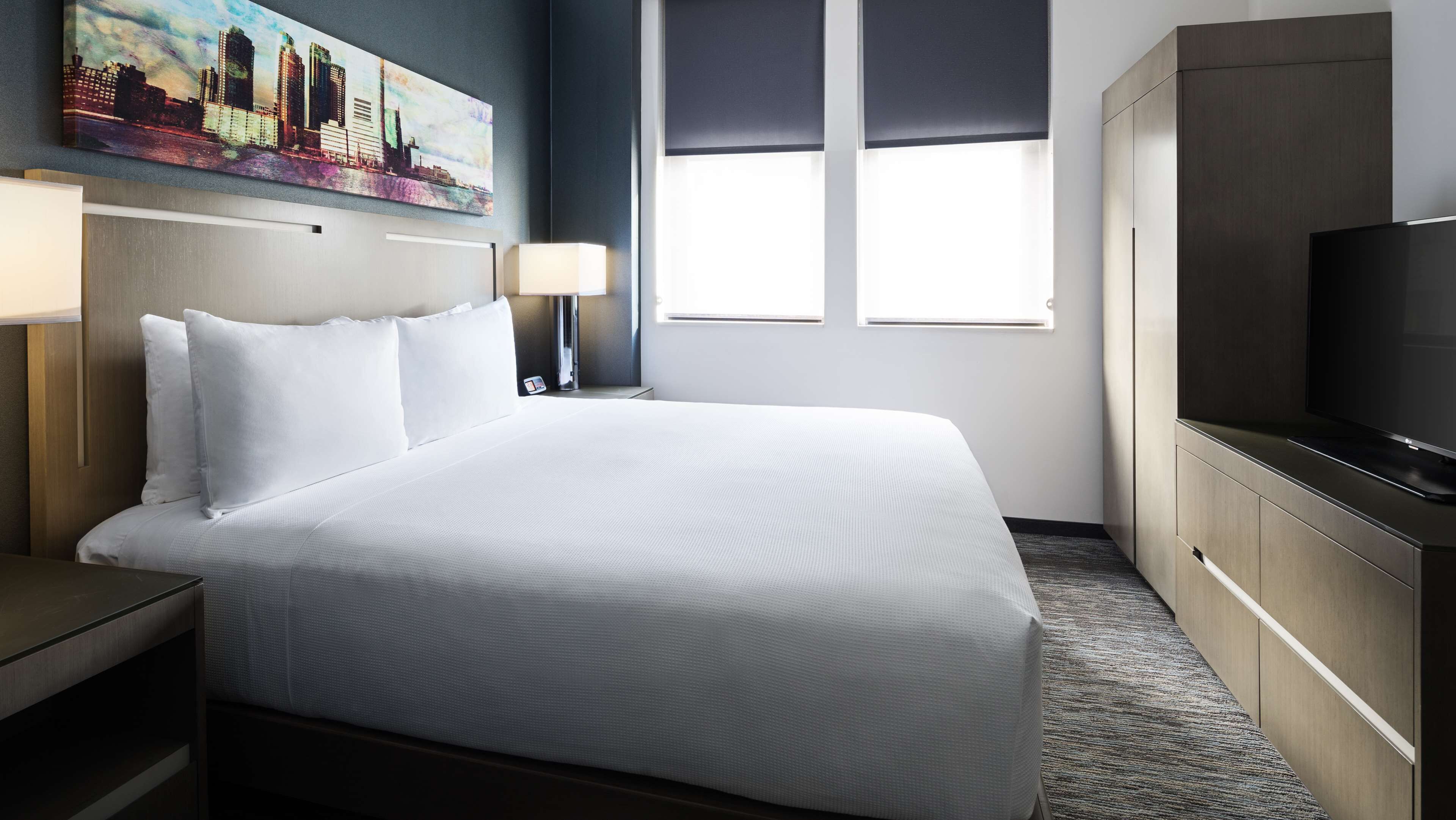 A hotel room with a large bed, a TV, a desk, and a painting on the wall.