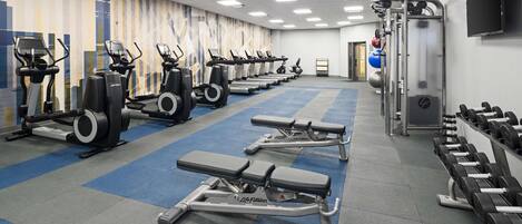 Une salle de sport équipée de tapis de course, de vélos elliptiques, de bancs et de matériel d'haltérophilie.