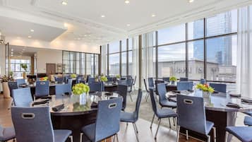 A modern conference room with round tables, blue chairs, and large windows offering city views.