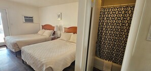 A hotel room with two beds, a shower curtain, and a small window with an air conditioning unit. - Fairview Inn (Fairview)