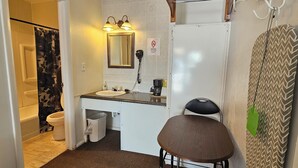 A small bathroom with a toilet, sink, and mirror. There is a chair and a shower curtain.