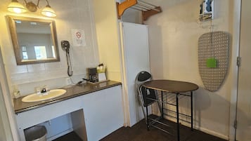 A bathroom with a sink, mirror, hairdryer, and a small table.