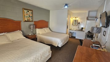 Hotellihuone, jossa on kaksi sänkyä, pieni työpöytä, peili ja televisio.