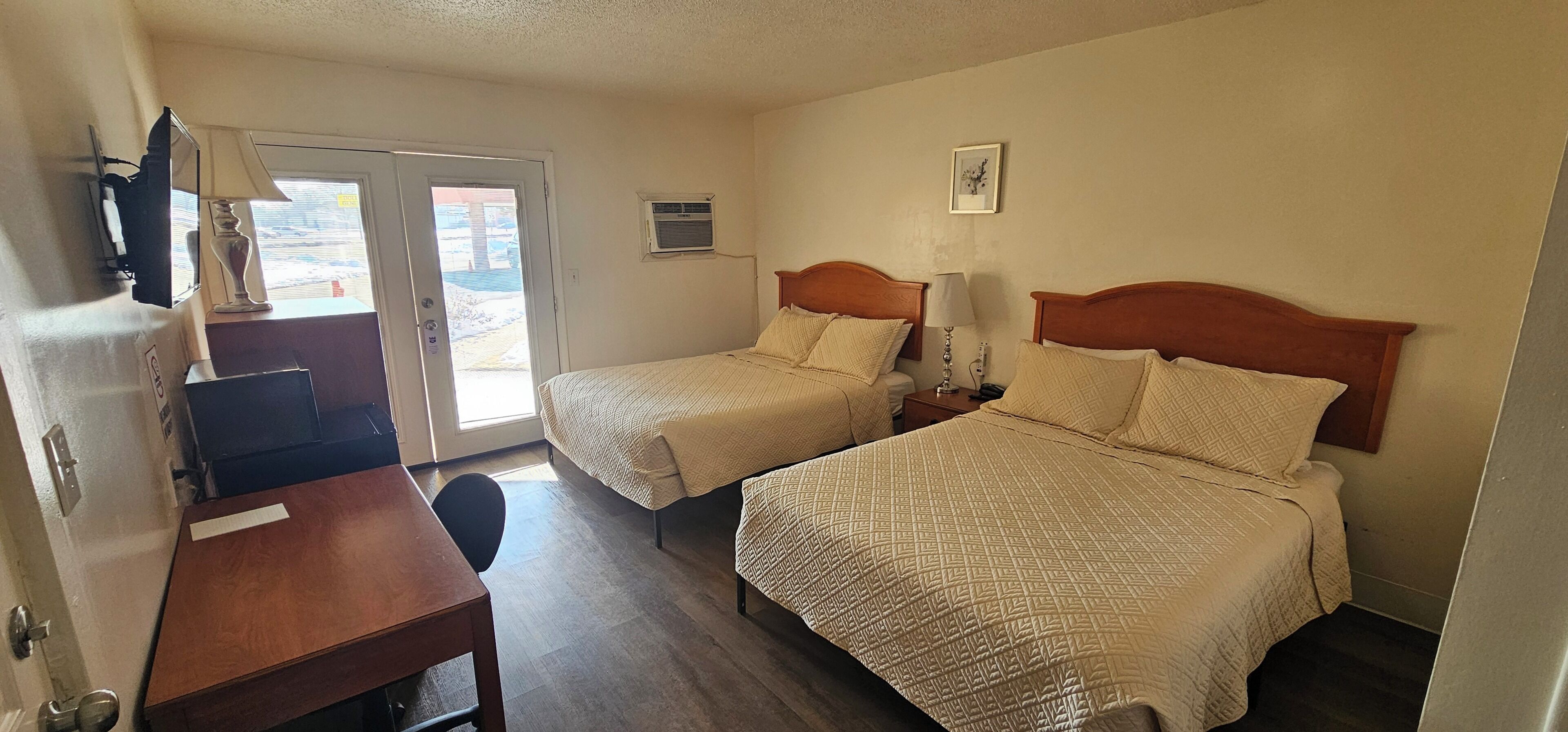A hotel room with two beds, a desk, a chair, a lamp, and a picture on the wall.