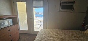 A bedroom with a bed, a dresser, a door leading to a balcony, and a wall-mounted air conditioning unit. - Fairview Inn (Fairview)